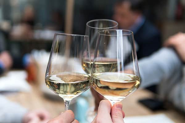 Drei amüsierte Personen stoßen mit Weißweingläsern im Restaurant in Gemünden an